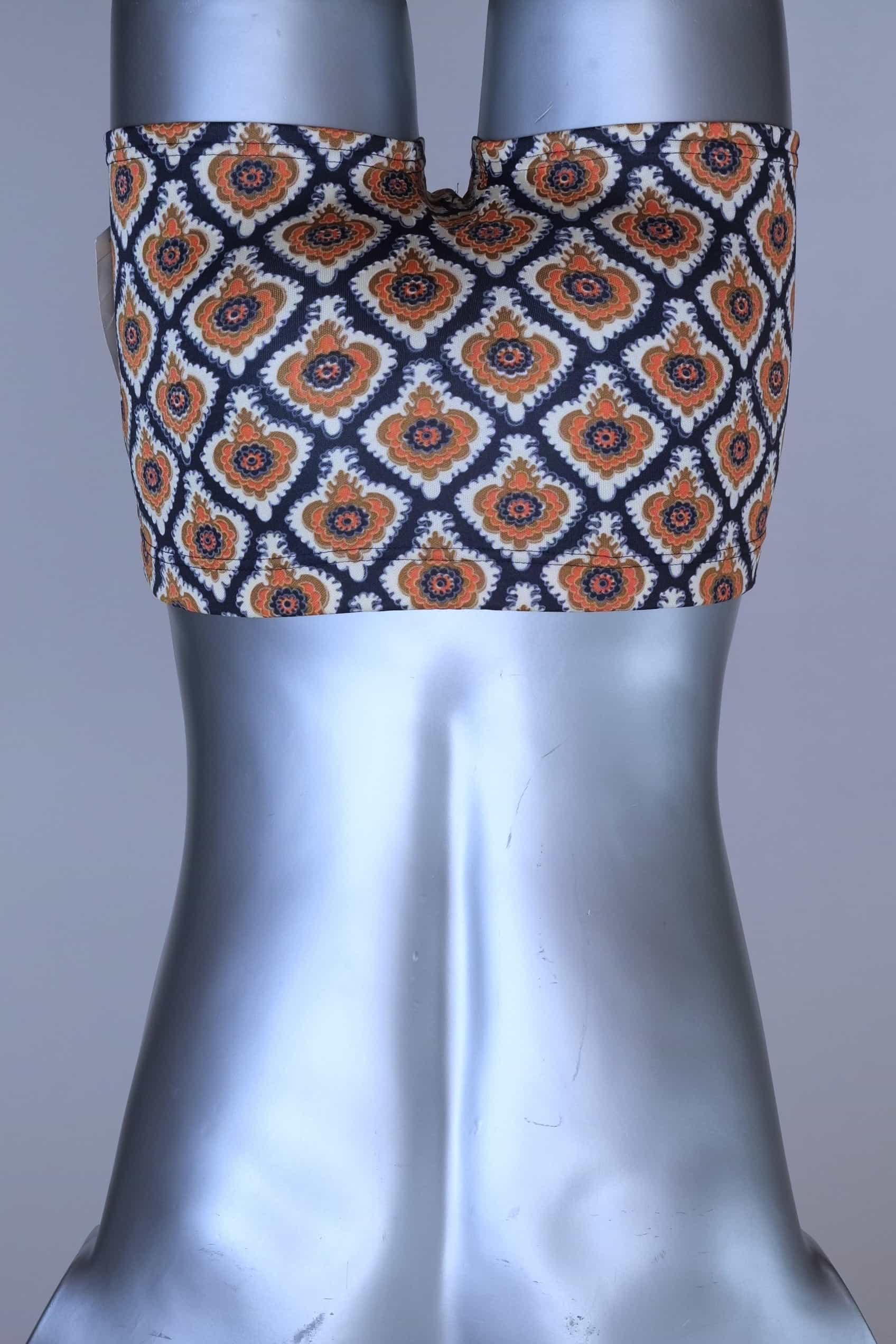 Back view of vintage 60s Lahco swim trunks in navy with an allover brown, orange, and cream geometric medallion print, featuring a zip pocket and original brand tag.