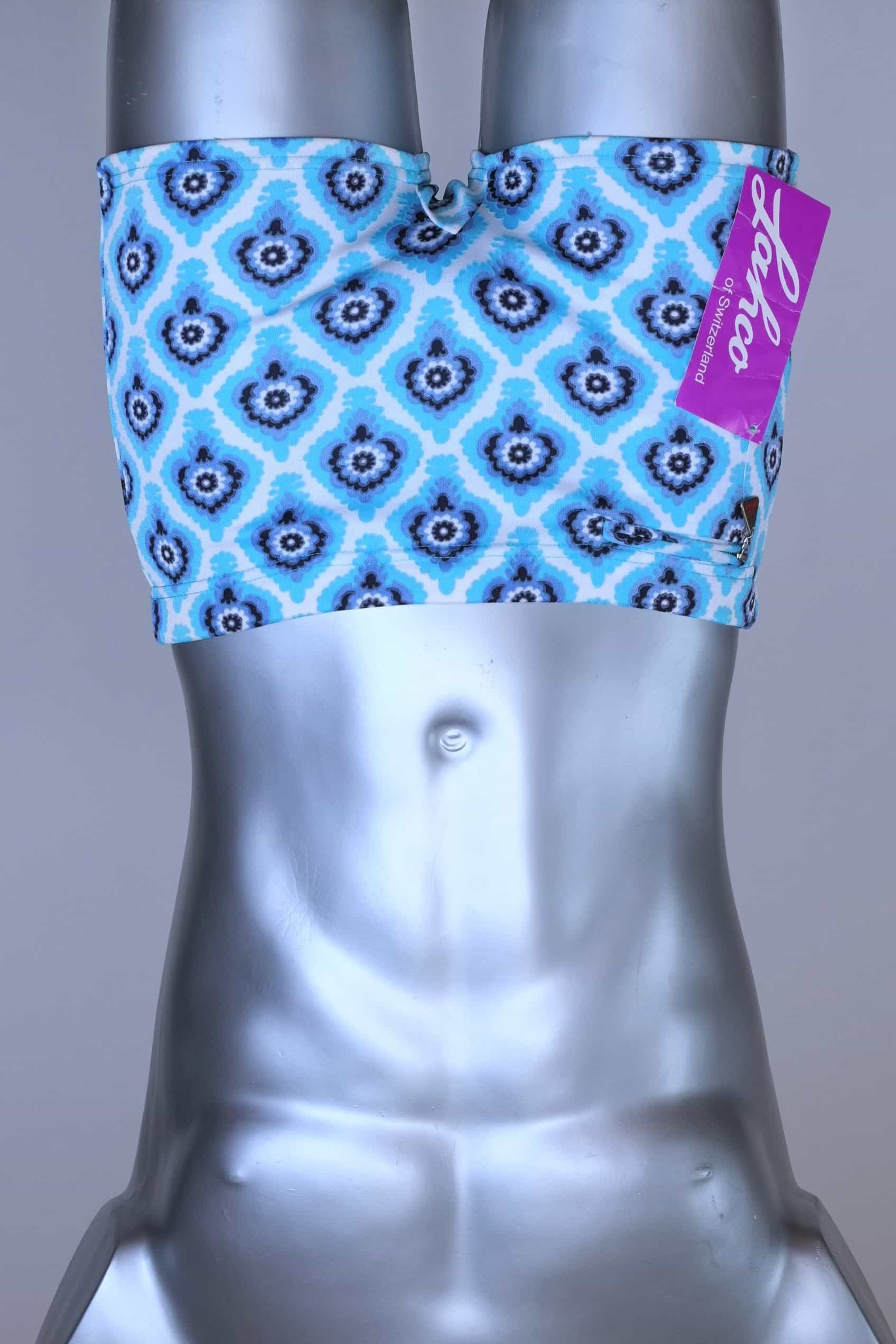 Front view of vintage 60s Lahco swim trunks in icy blue with a repeating dark blue and white geometric medallion pattern, featuring a zip pocket and brand tag.