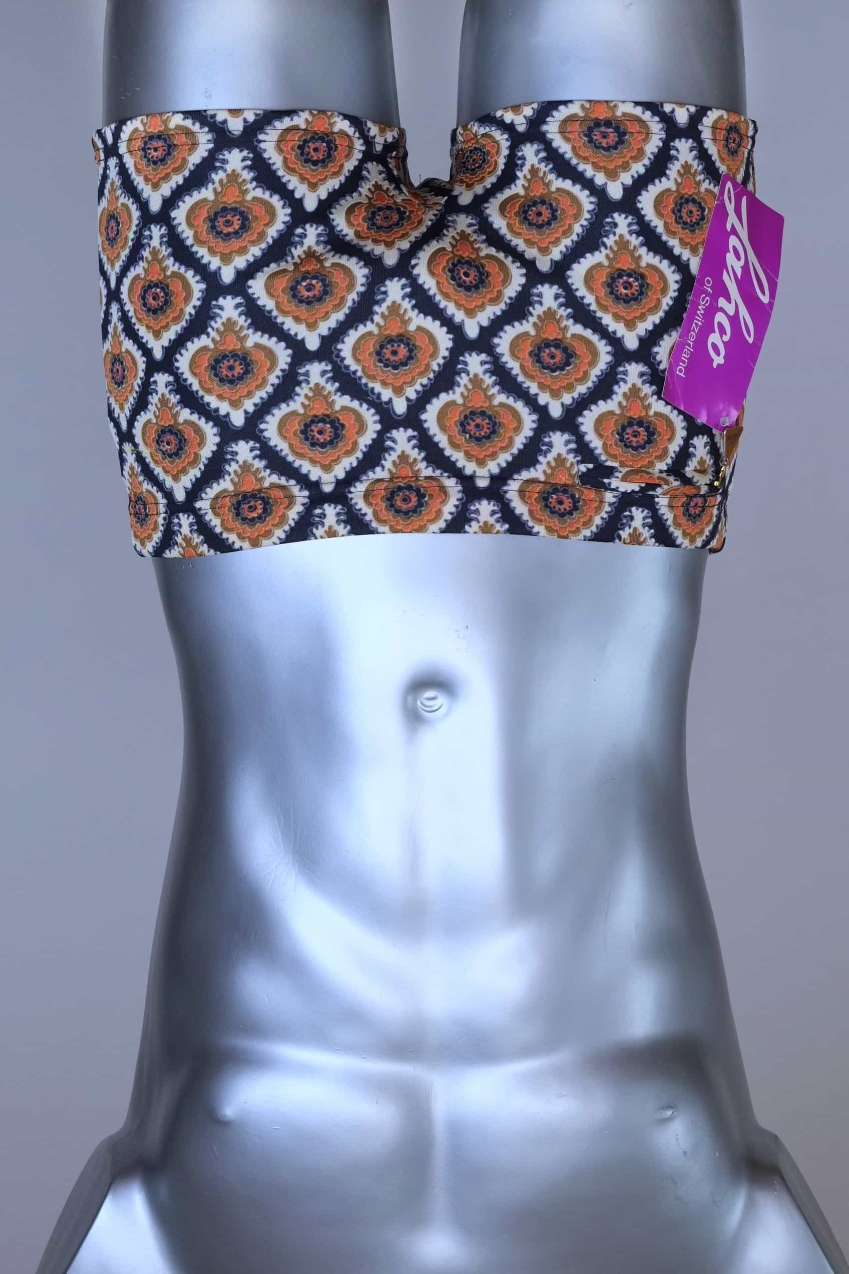Front view of vintage 60s Lahco swim trunks in navy with an allover brown, orange, and cream geometric medallion print, featuring a zip pocket and original brand tag.