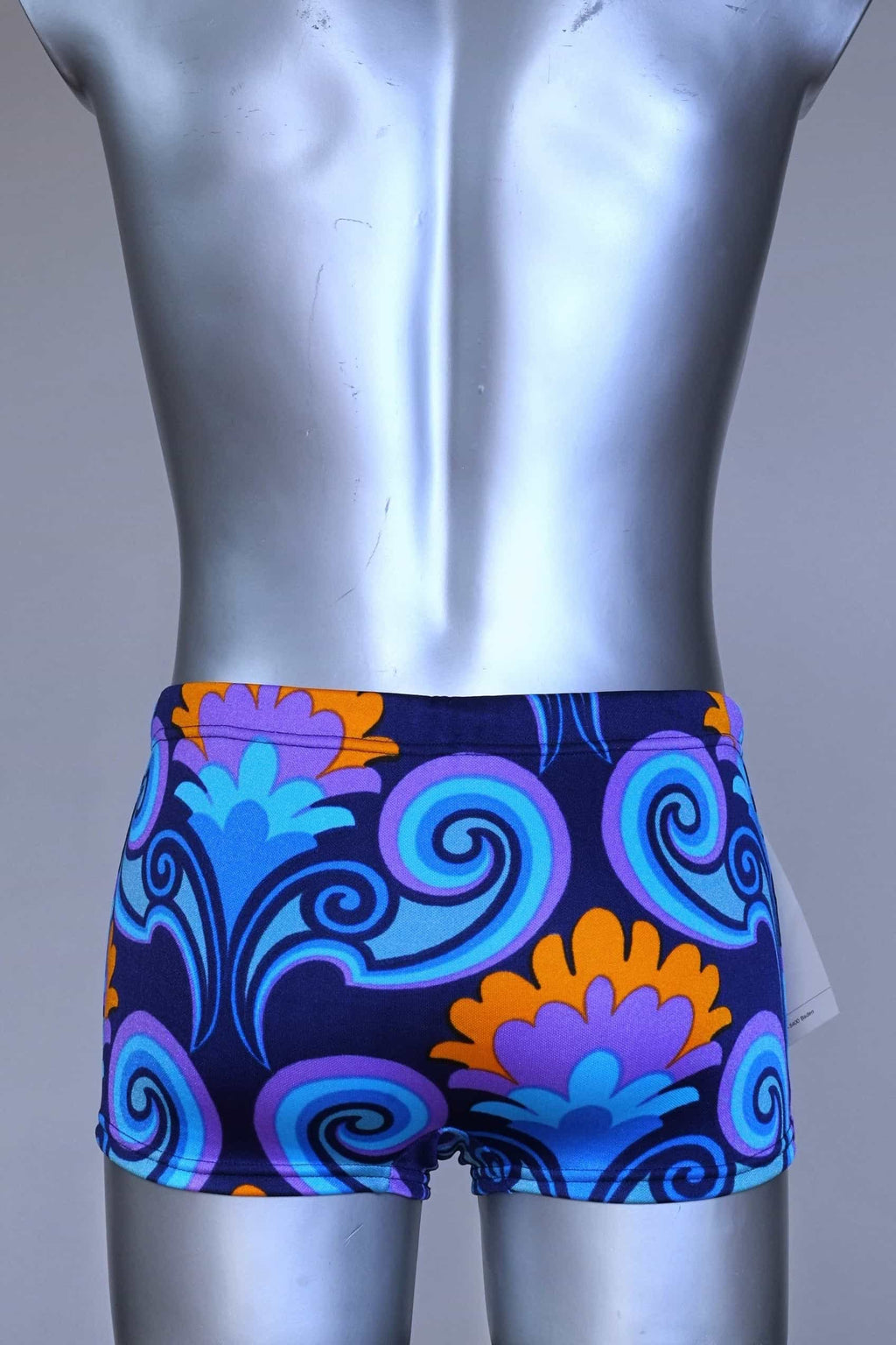 Back view of LAHCO vintage 60s square-cut swim trunks in a blue, purple, and orange psychedelic floral print, shown on a mannequin with original tag.