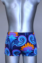 Back view of LAHCO vintage 60s square-cut swim trunks in a blue, purple, and orange psychedelic floral print, shown on a mannequin with original tag.