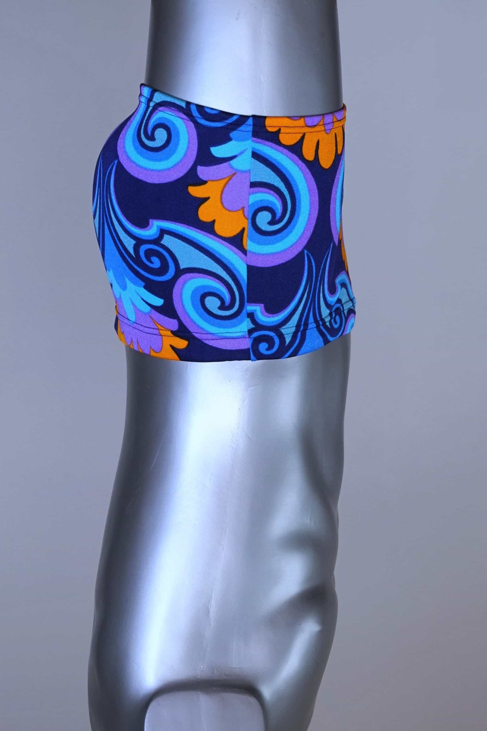 Side view of LAHCO vintage 60s square-cut swim trunks in a blue, purple, and orange psychedelic floral print, shown on a mannequin with original tag.