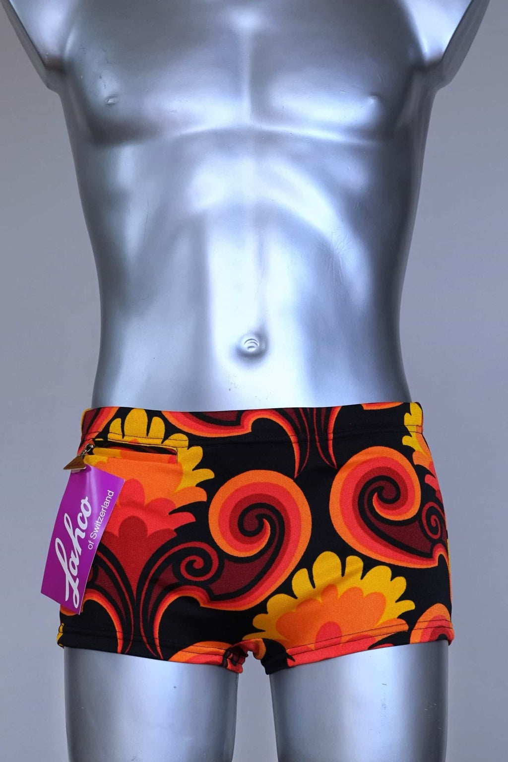 Front view of LAHCO vintage 60s square-cut swim trunks in a red, orange, and yellow psychedelic print, shown on a mannequin with original tag.
