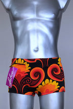 Front view of LAHCO vintage 60s square-cut swim trunks in a red, orange, and yellow psychedelic print, shown on a mannequin with original tag.