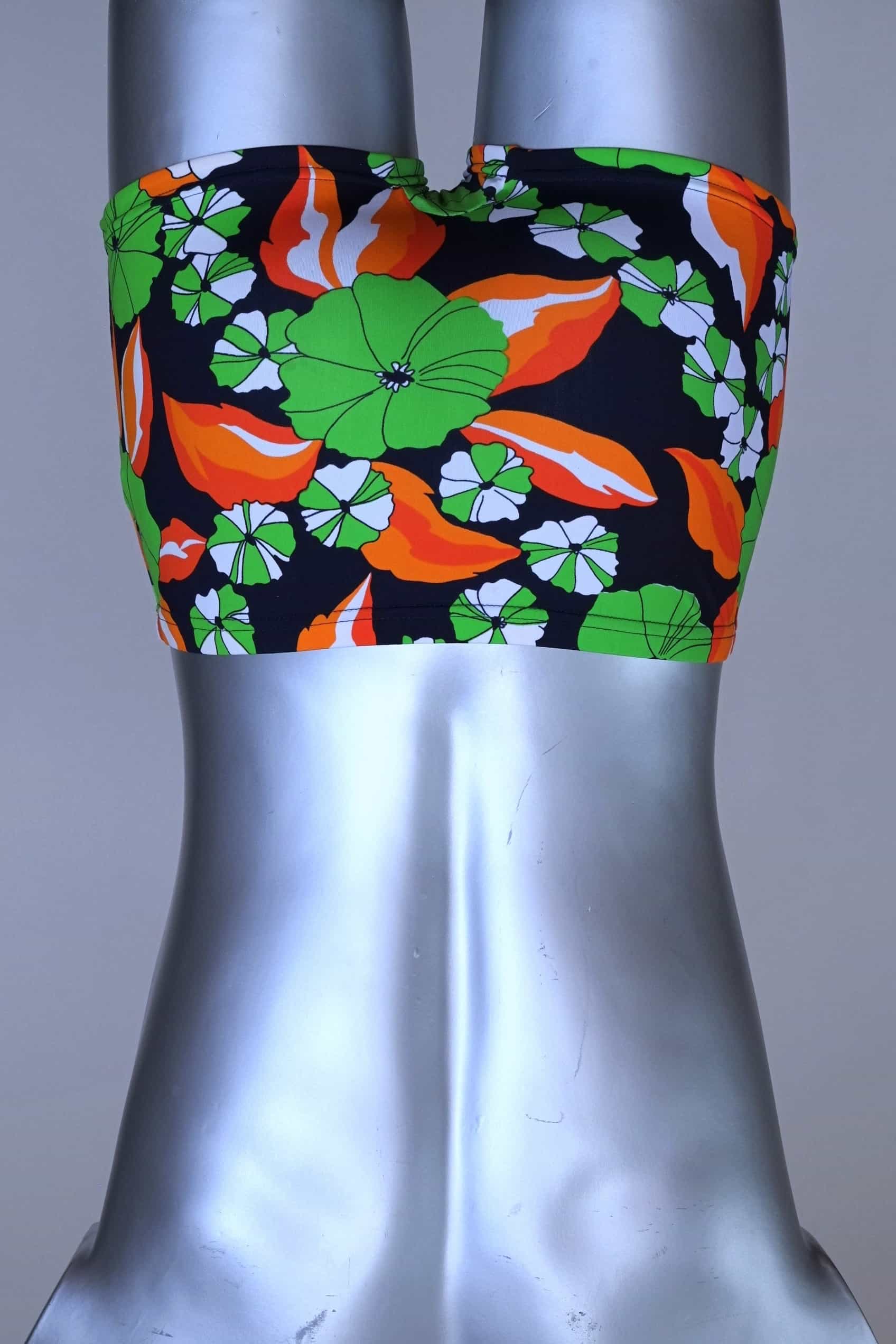 Back view of LAHCO vintage 1960s men's swim trunks on a silver mannequin. The trunks are black with a vibrant green, orange, and white floral pattern.
