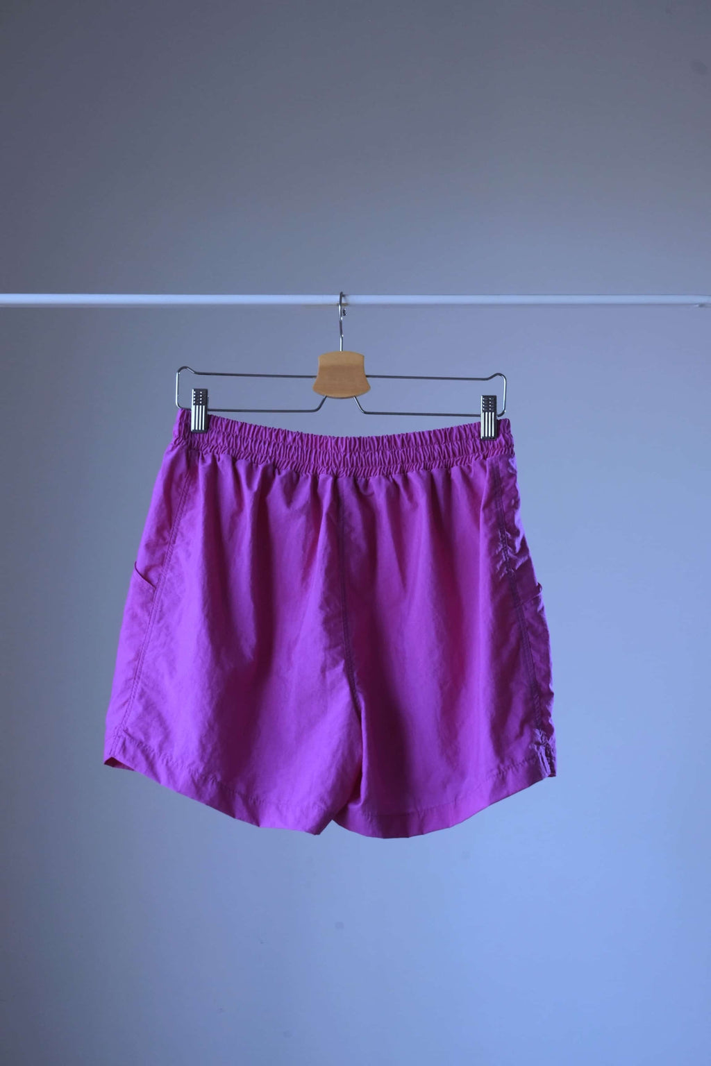 Rear view of a pair of magenta vintage Löffler shorts with a small logo on the left leg, hanging on a hanger