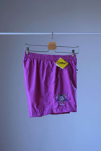 Side view of a pair of magenta vintage Löffler shorts with a small logo on the left leg, hanging on a hanger, a yellow Löffler hang tag is visible.