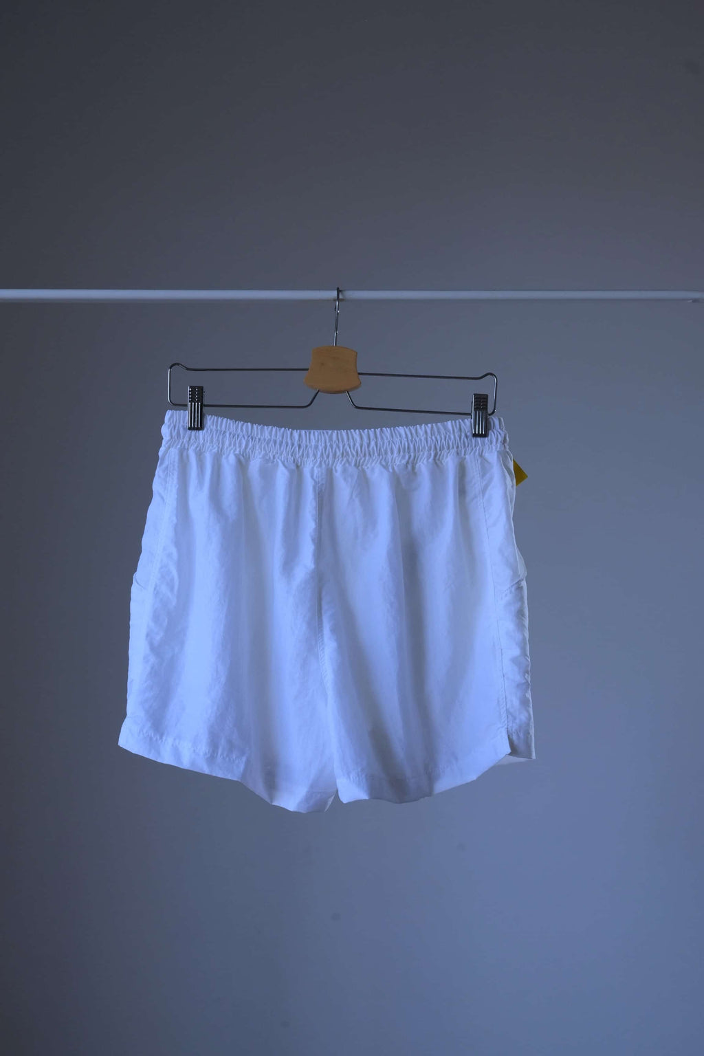Rear view of a pair of white vintage Löffler shorts with a small logo on the left leg, hanging on a hanger