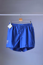 Front view of a pair of blue vintage Löffler shorts with a small logo on the left leg, hanging on a hanger.