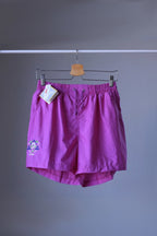 Front view of a pair of magenta vintage Löffler shorts with a small logo on the left leg, hanging on a hanger.