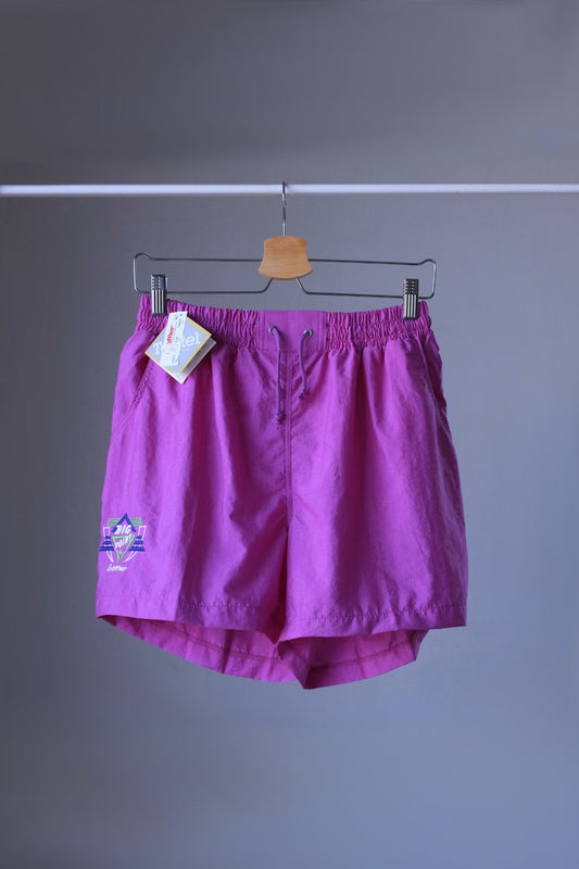 Front view of a pair of magenta vintage Löffler shorts with a small logo on the left leg, hanging on a hanger.