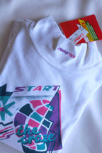 Flat lay of the white Löffler mock neck top showing the pink Transtex collar embroidery, the “Start the Craze” graphic and the red Löffler Transtex hang tag