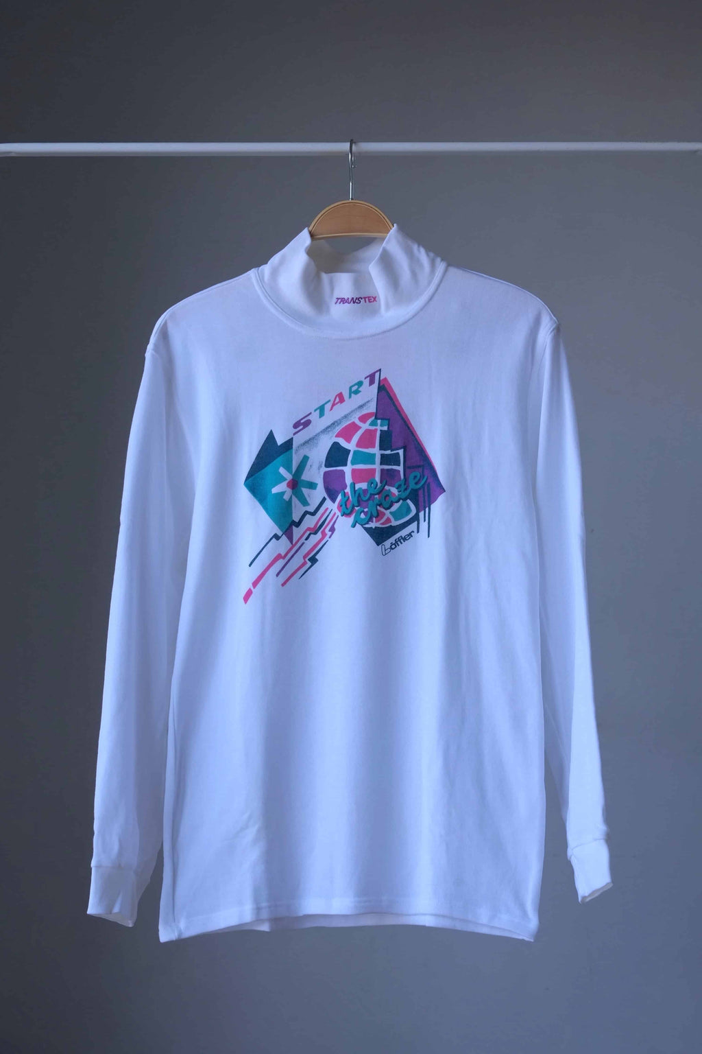 Front view of white Löffler 90s mock neck long-sleeve tennis top with a pink, teal and purple “Start the Craze” graphic and Transtex collar embroidery