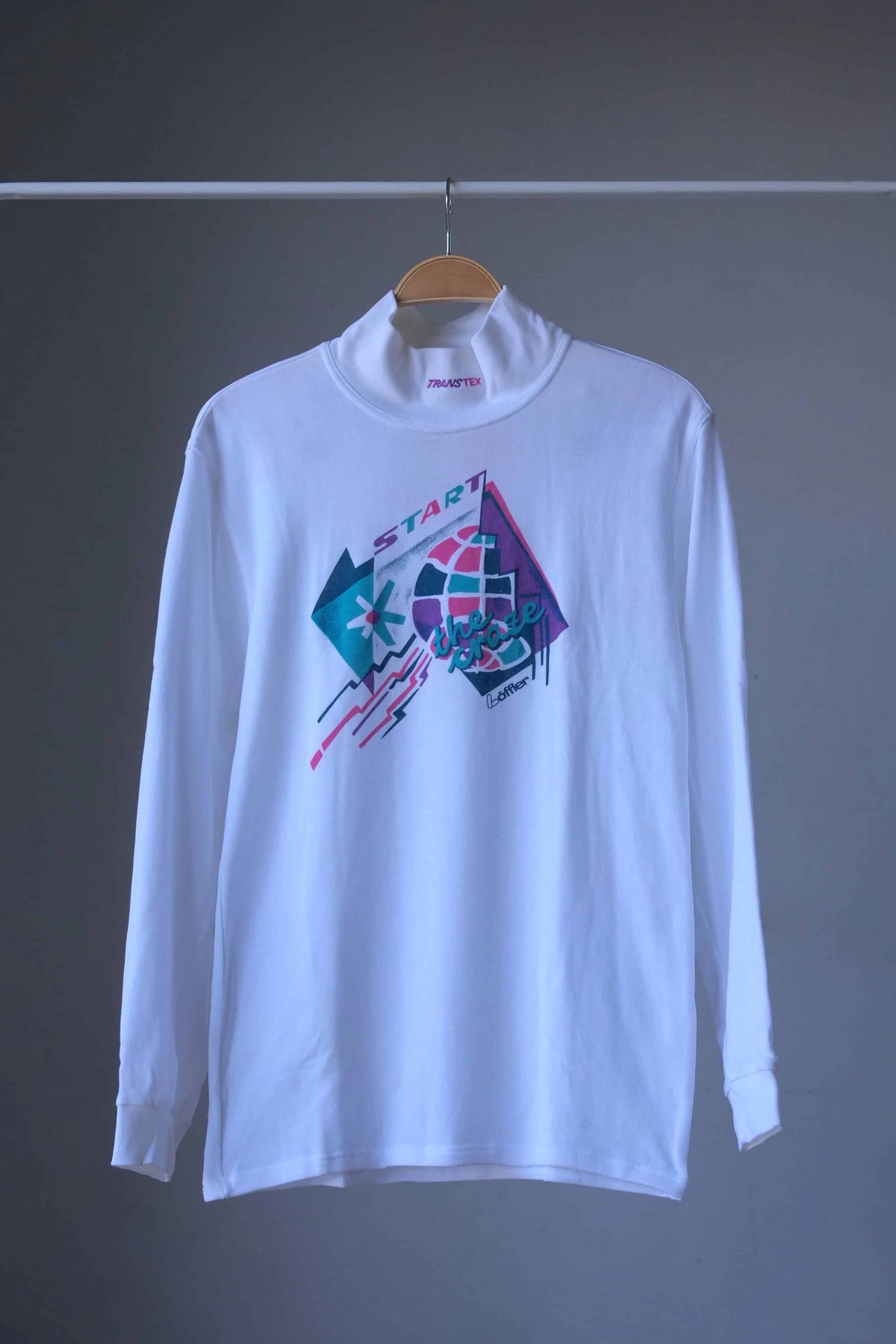 Front view of white Löffler 90s mock neck long-sleeve tennis top with a pink, teal and purple “Start the Craze” graphic and Transtex collar embroidery