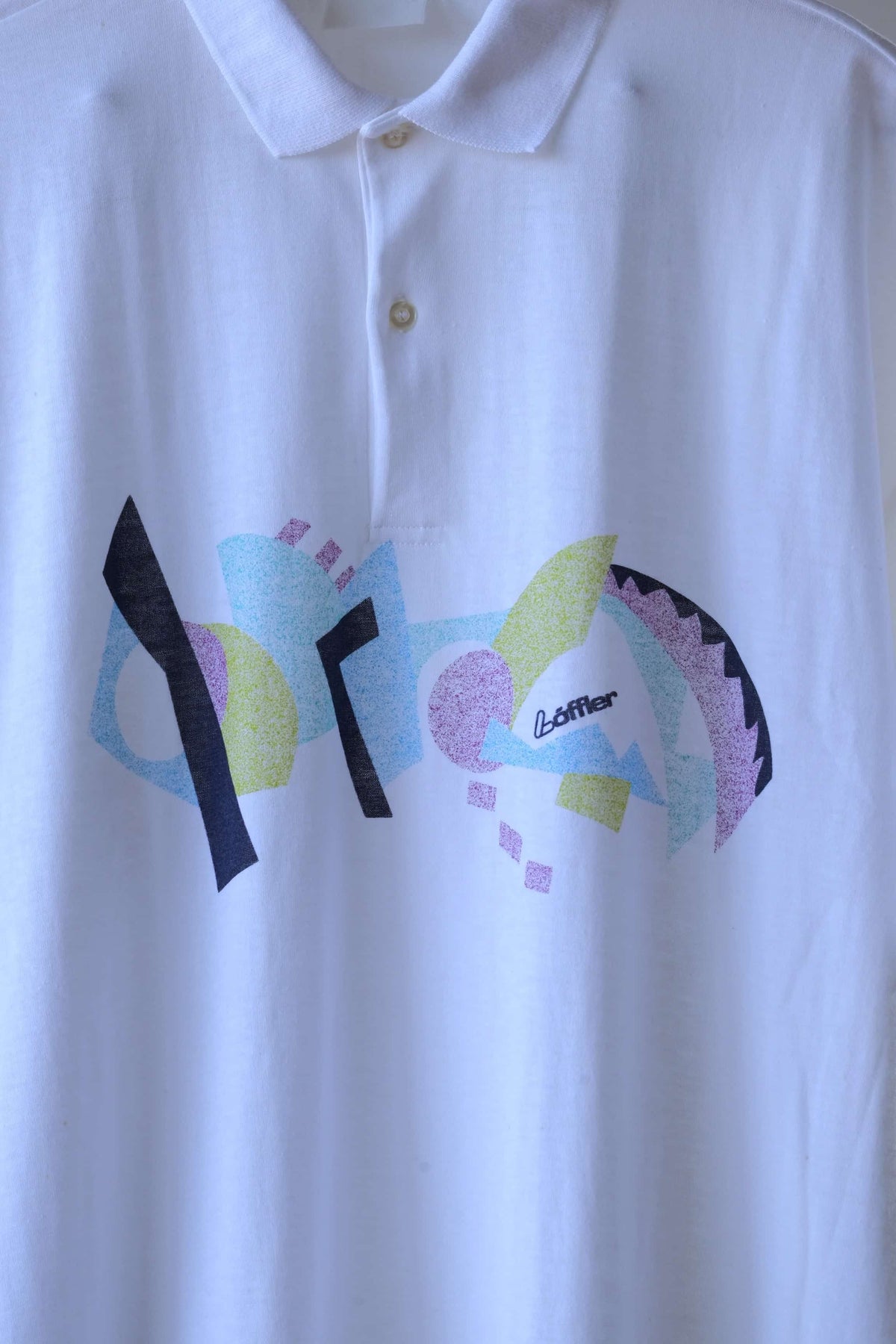 Close-up of the Löffler Memphis print on a white 90s polo, with geometric shapes, a Löffler logo and a two-button placket