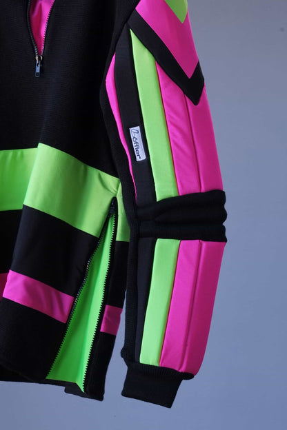 Close-up detail of the sleeve of a black Löffler ski sweater, featuring neon pink and green padded sections, a black zipper, and the Löffler brand label.