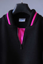 Close-up of the front of a black Löffler ski sweater, featuring a padded collar with pink accents and inset, and a black zipper. The label can be seen with the word Löffler on it.