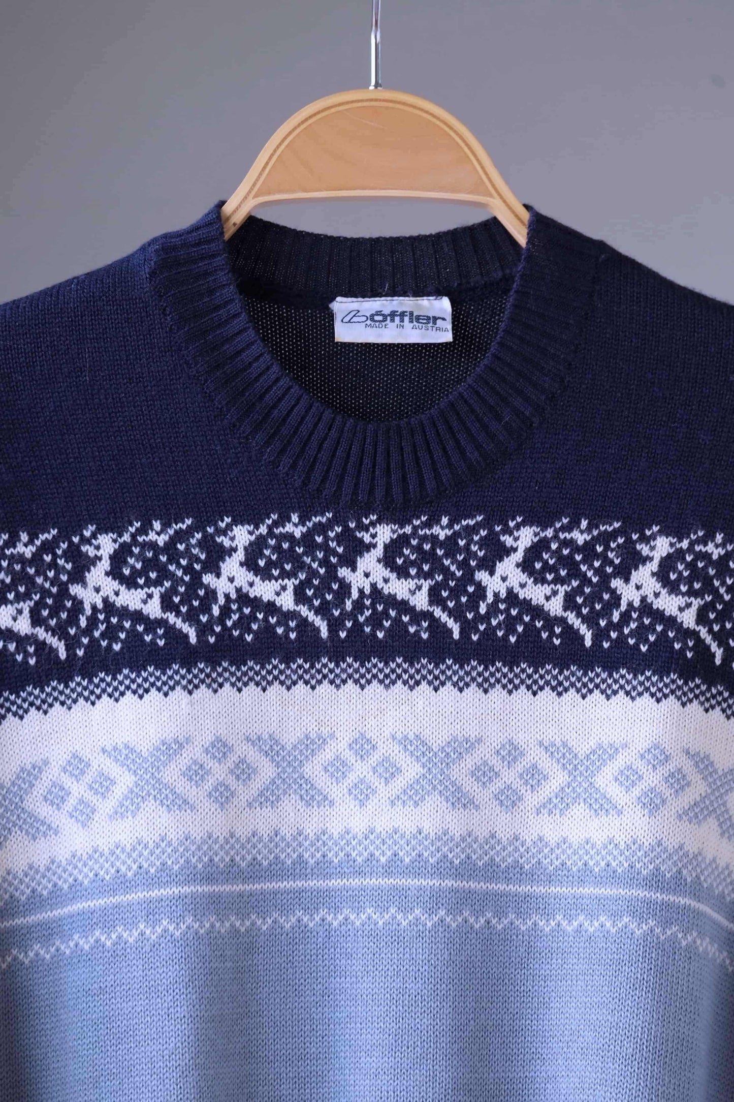 Close up of a Löffler burgundy and gray wool blend sweater featuring a white Nordic pattern with reindeer and snowflake motifs, hanging on a wooden hanger against a plain background.