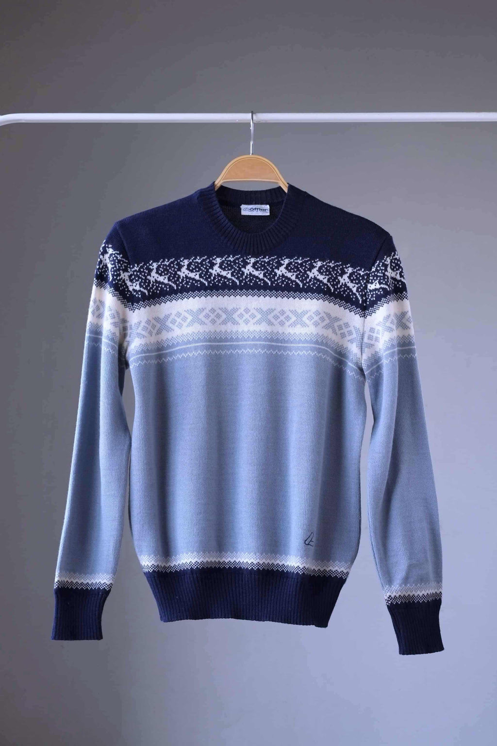 Löffler brand navy and light blue wool blend sweater featuring a white Nordic pattern with reindeer and snowflake motifs, hanging on a wooden hanger against a plain background.