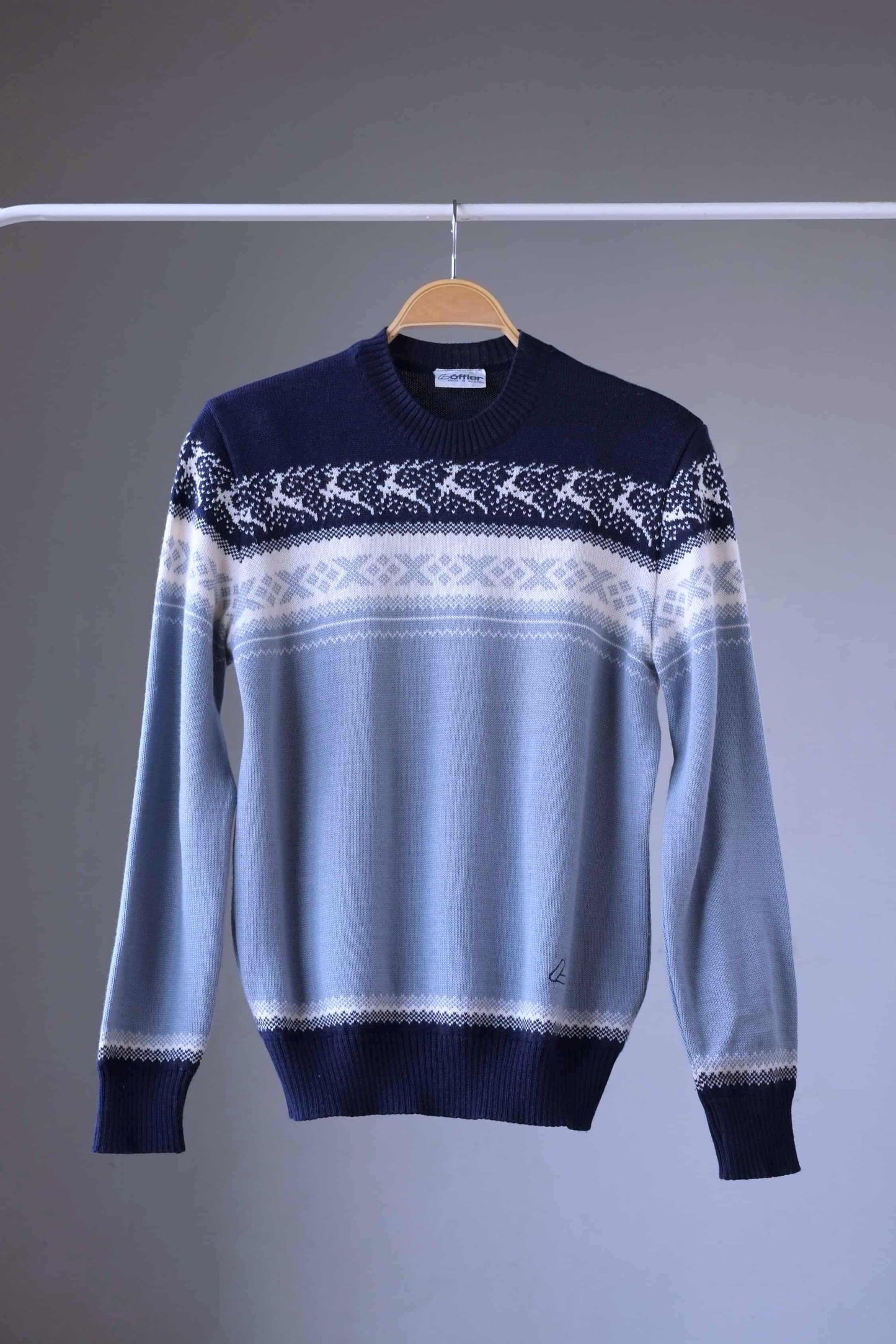 Löffler brand navy and light blue wool blend sweater featuring a white Nordic pattern with reindeer and snowflake motifs, hanging on a wooden hanger against a plain background.