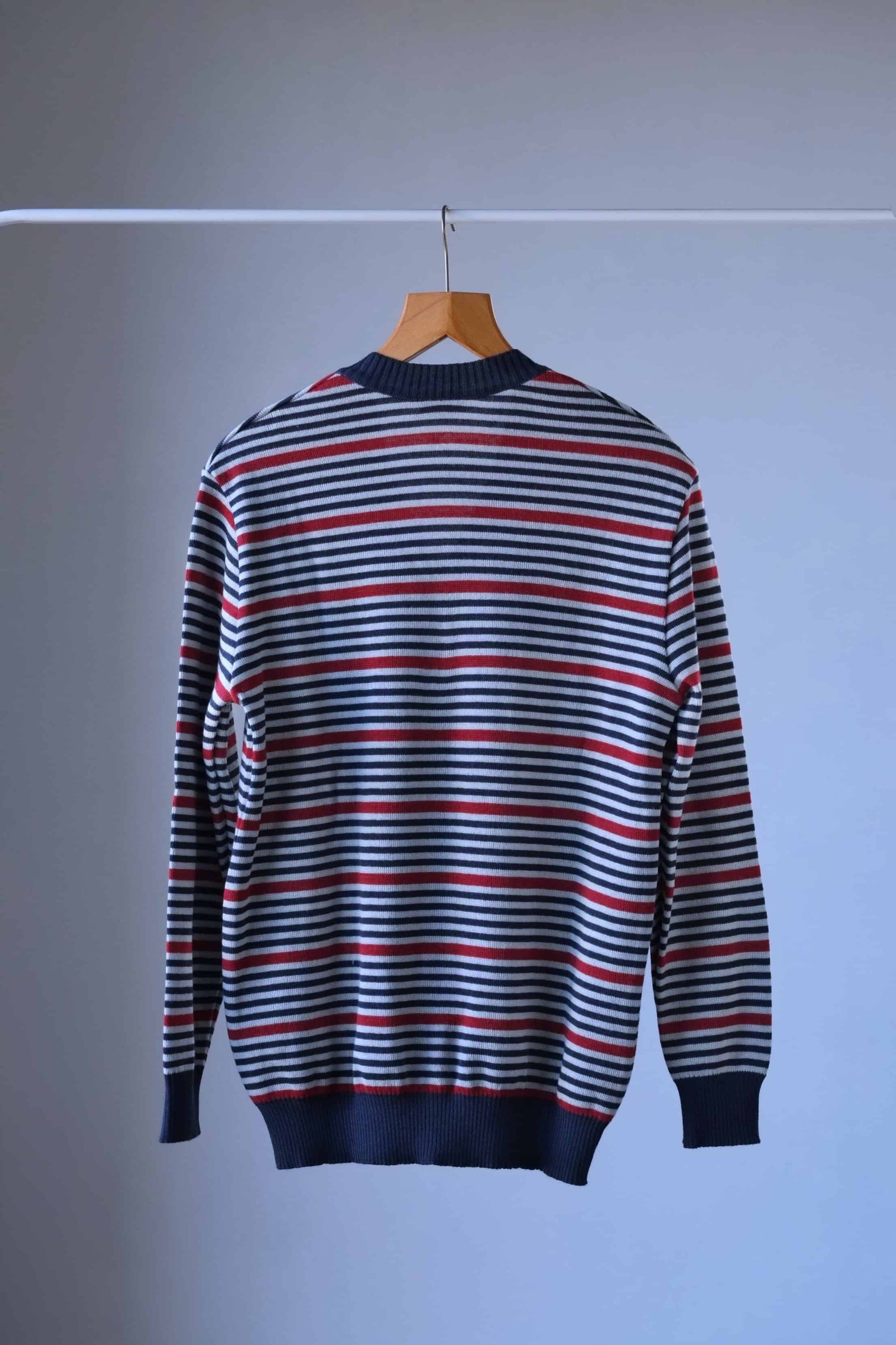 Back view of a Loffler vintage sweater with horizontal stripes in shades of blue, red, and white. It has a v-neck and is hanging on a wooden hanger.