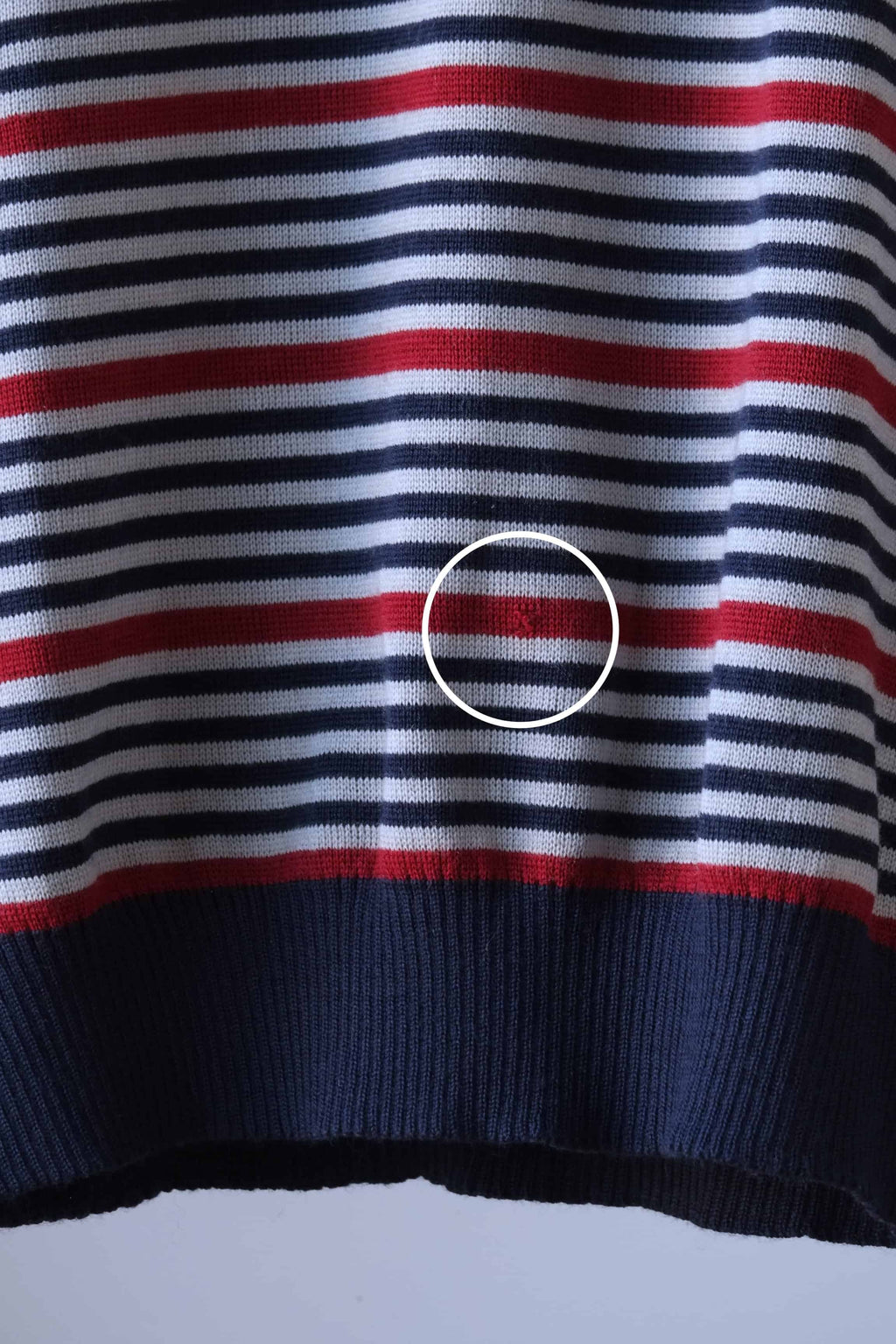 Close-up of a vintage Löffler striped V-neck sweater, highlighting a hole on the front. The sweater features horizontal stripes in burgundy, navy blue, grey, with a ribbed hem and cuffs. A white circle marks the repaired area for visibility.