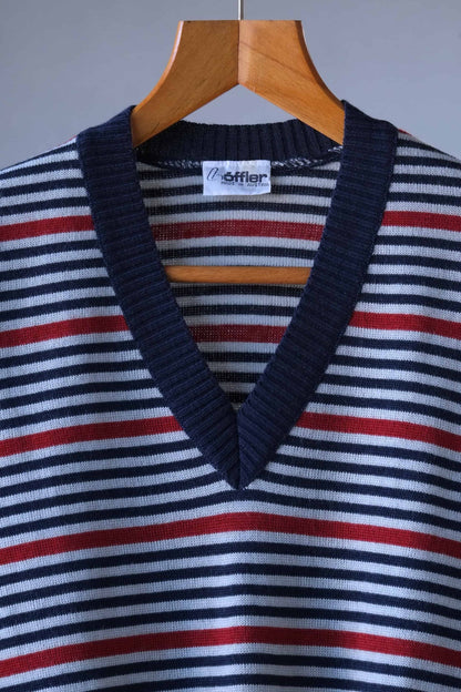 Detail shot of the Löffler brand tag on a v-neck sweater with horizontal stripes in shades of blue, red, and grey.