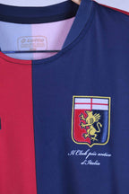 Close-up shot of the Genoa CFC club crest embroidered on the navy blue fabric section, showing a golden griffin beneath a white shield with a red cross. Script beneath the crest reads "Il Club più antico d'Italia".