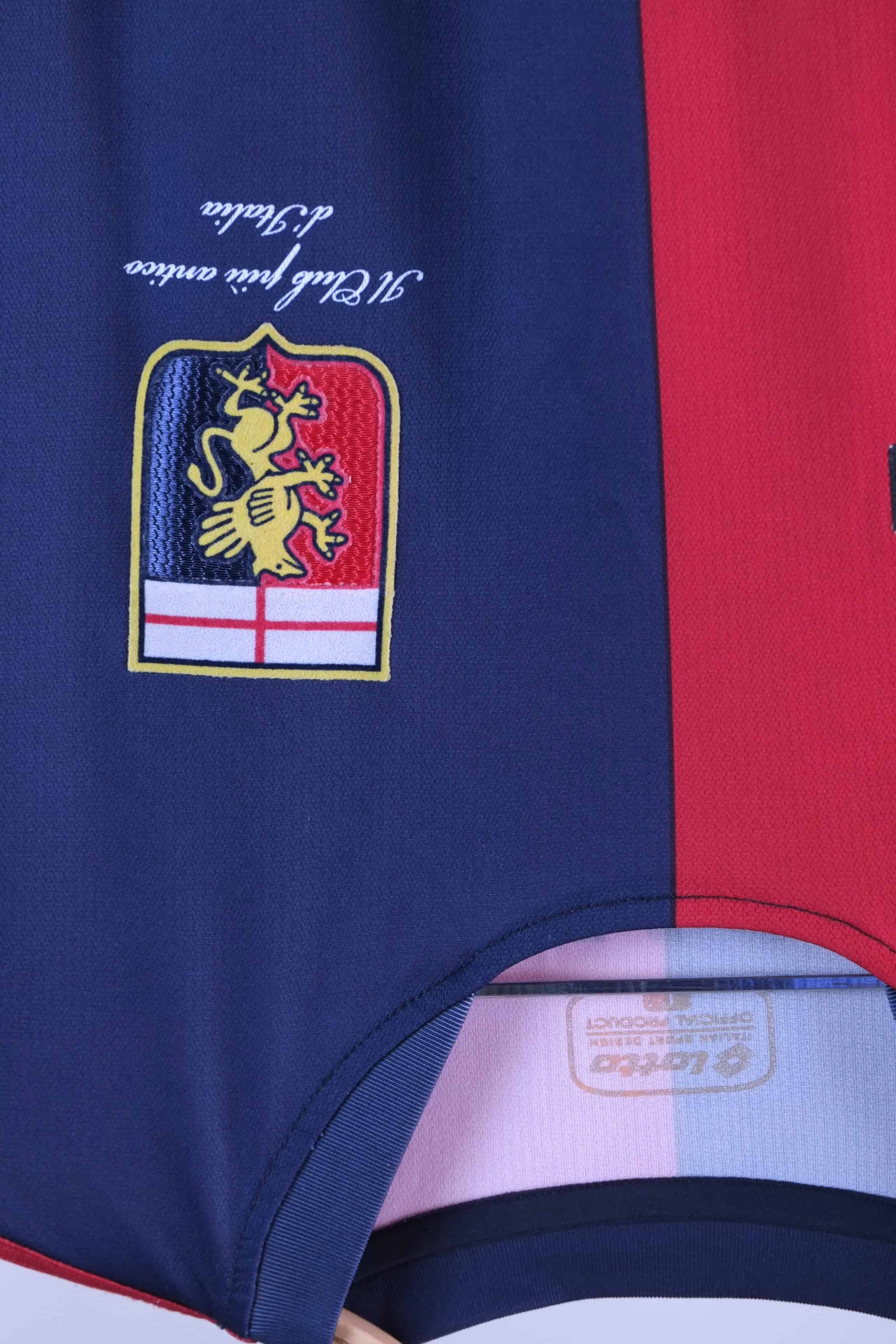 Close-up shot of the Genoa CFC club crest embroidered on the navy blue fabric section, showing a golden griffin beneath a white shield with a red cross. Script beneath the crest reads "Il Club più antico d'Italia".