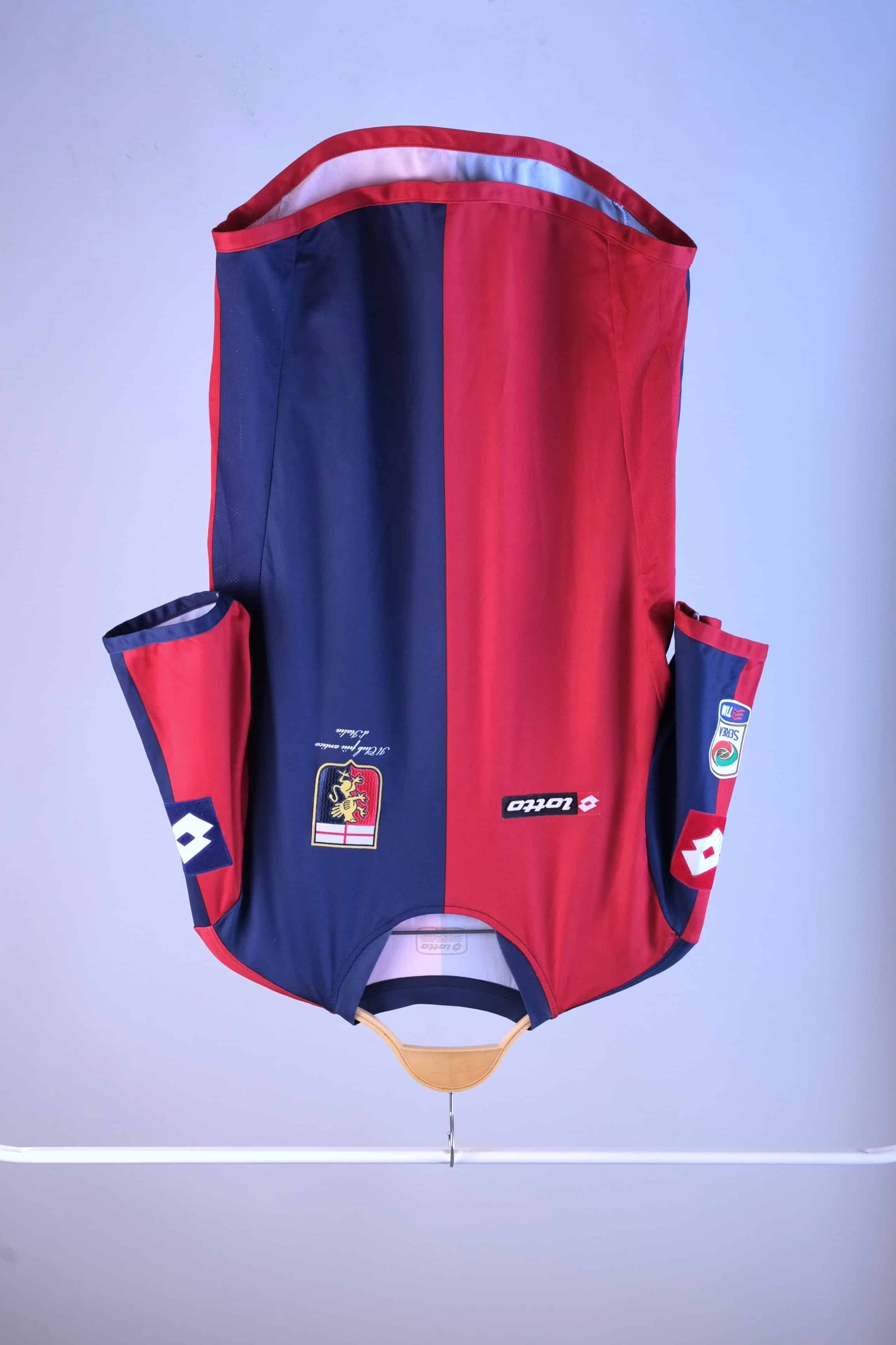 Front view of a red and navy blue vertically split football jersey hanging on a wooden hanger against a plain grey background. The jersey features a black "lotto" logo on the right breast, a club crest on the left breast, and a Serie A TIM patch on the right sleeve.