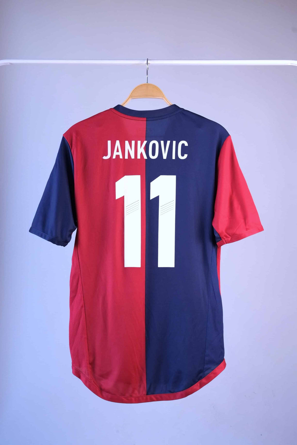 Back view of a red and navy blue vertically split football jersey hanging on a wooden hanger against a plain grey background. The name "JANKOVIC" and the number "11" are printed in large white text across the upper back.
