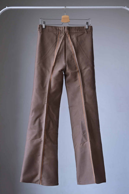 Back view of a pair of Lucky Paris 70's Vintage brown flared pants hanging on a hanger. The pants have a wide leg opening and feature orange stitching details.