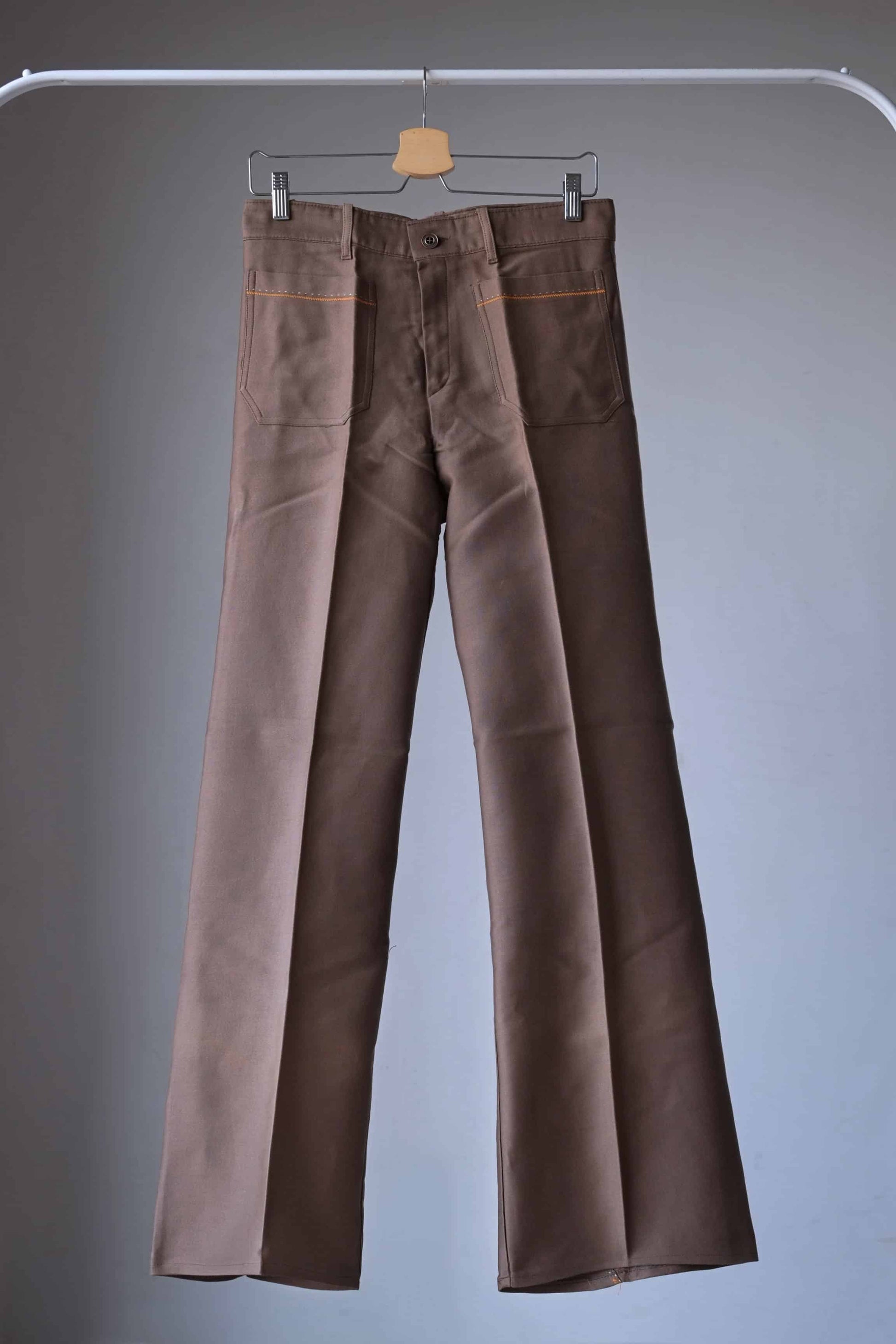 Lucky Paris 70's Vintage brown flared pants hanging on a hanger. The pants have a wide leg opening and feature orange stitching details.