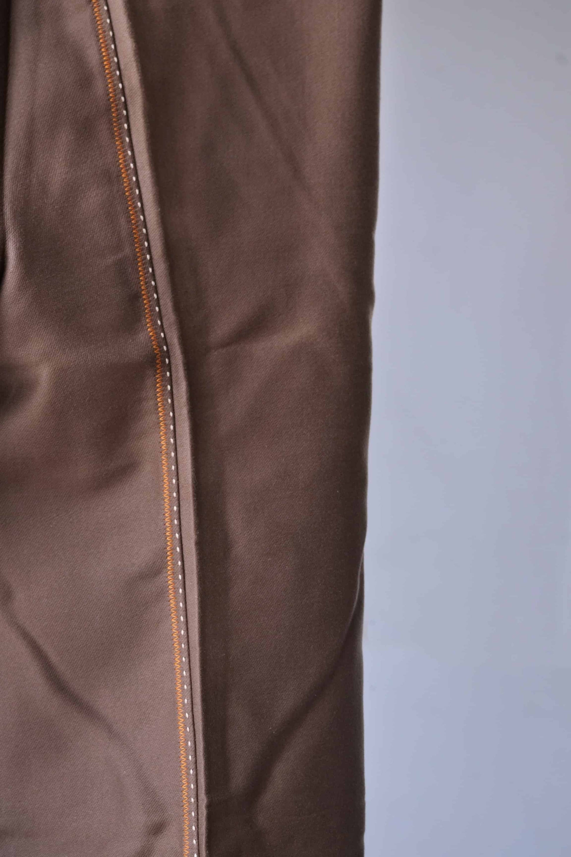 Close-up of brown fabric with orange stitching.
 The fabric appears soft and smooth with a slight sheen.