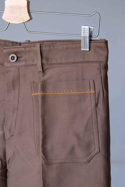 Close-up of the waistband and back pocket of brown pants.
 The pants feature a button closure, belt loops, and orange stitching detailing.