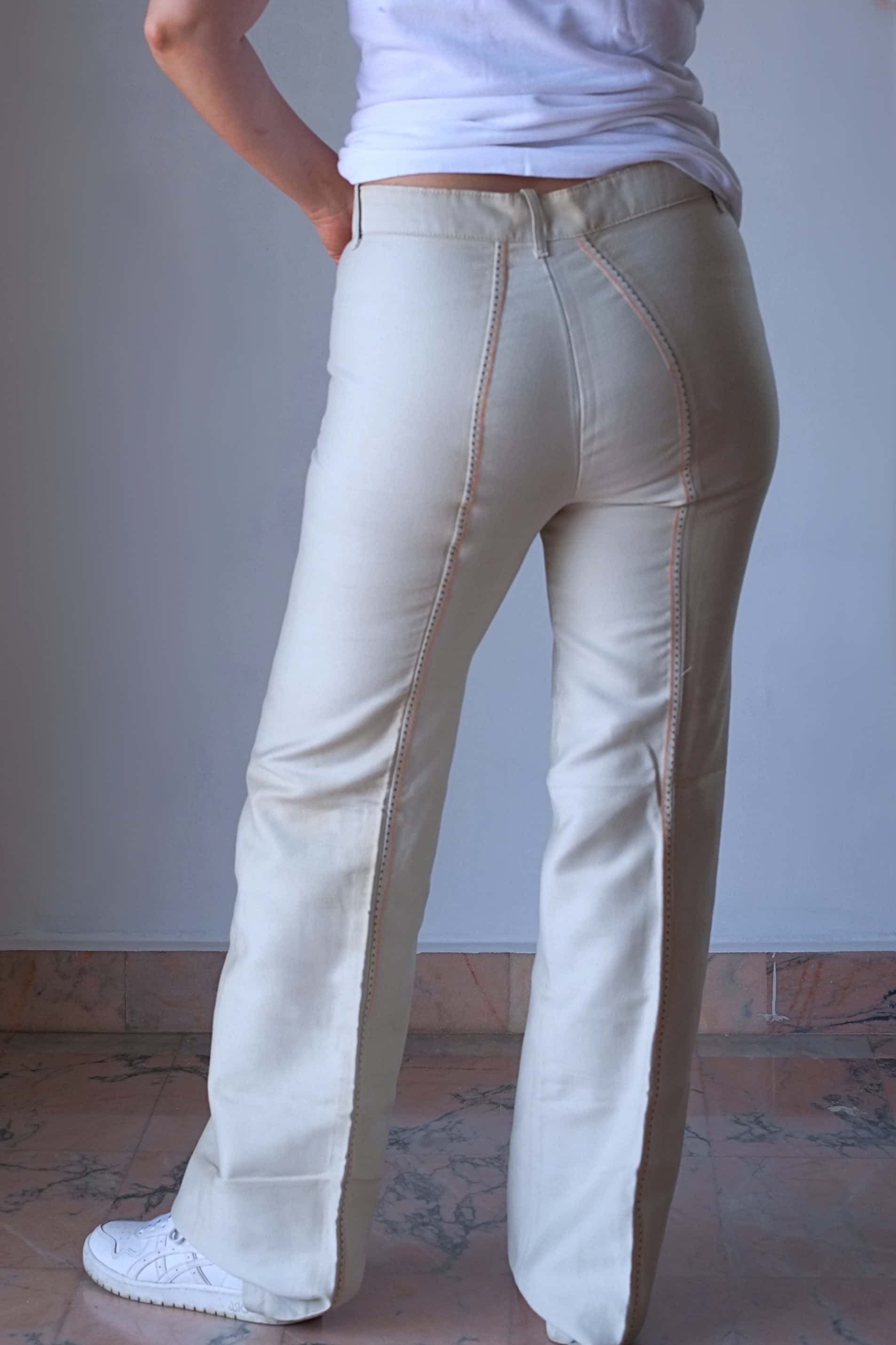 Back view of a model wearing 70's Vintage high-waisted cream flared pants paired with white sneakers, showcasing the vintage design and the stitching along the legs.