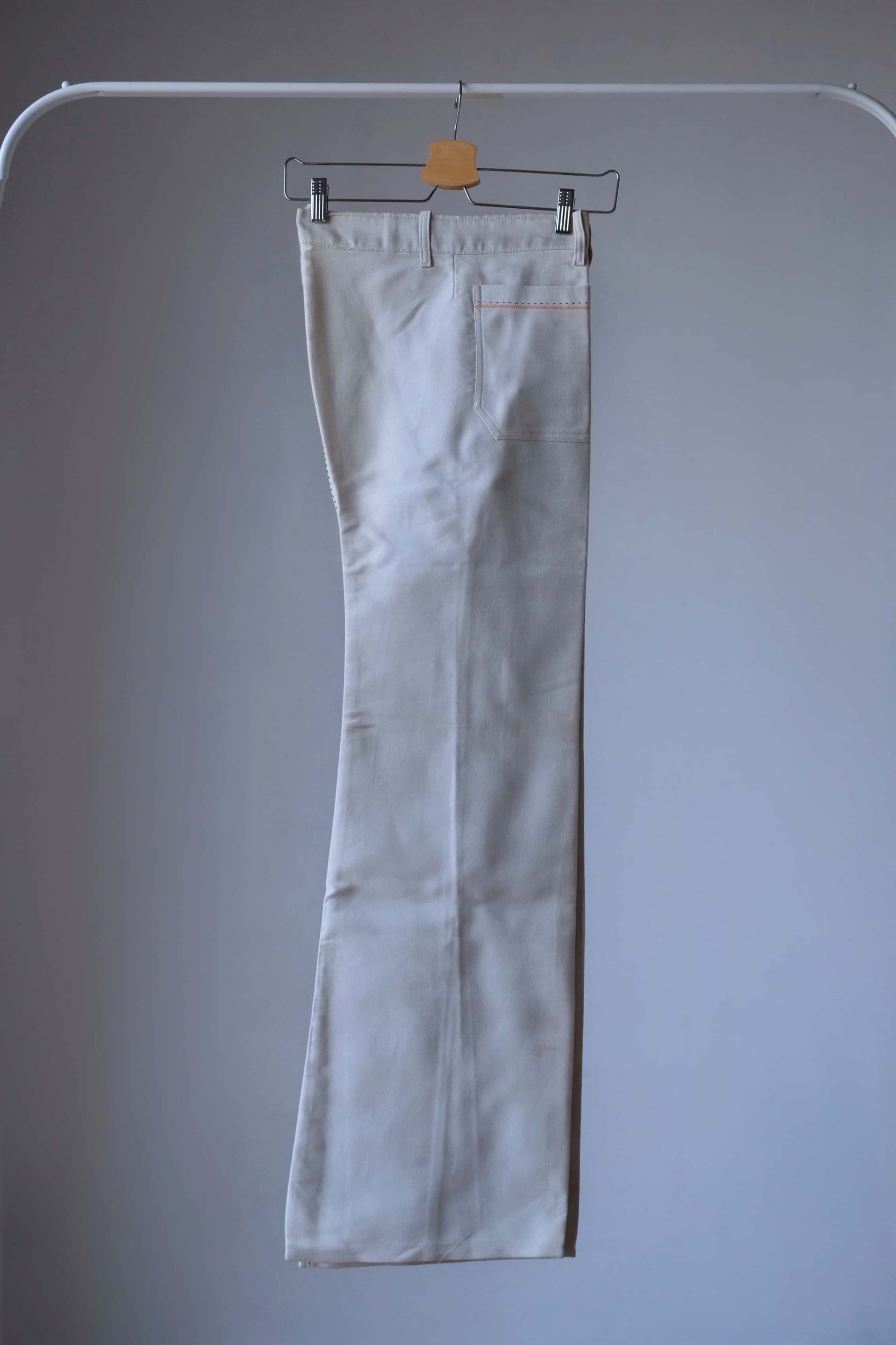 Lucky Paris 70's Vintage cream-colored flared pants hanging on a hanger. The pants have a wide leg opening and feature an orange-colored stitching detail.