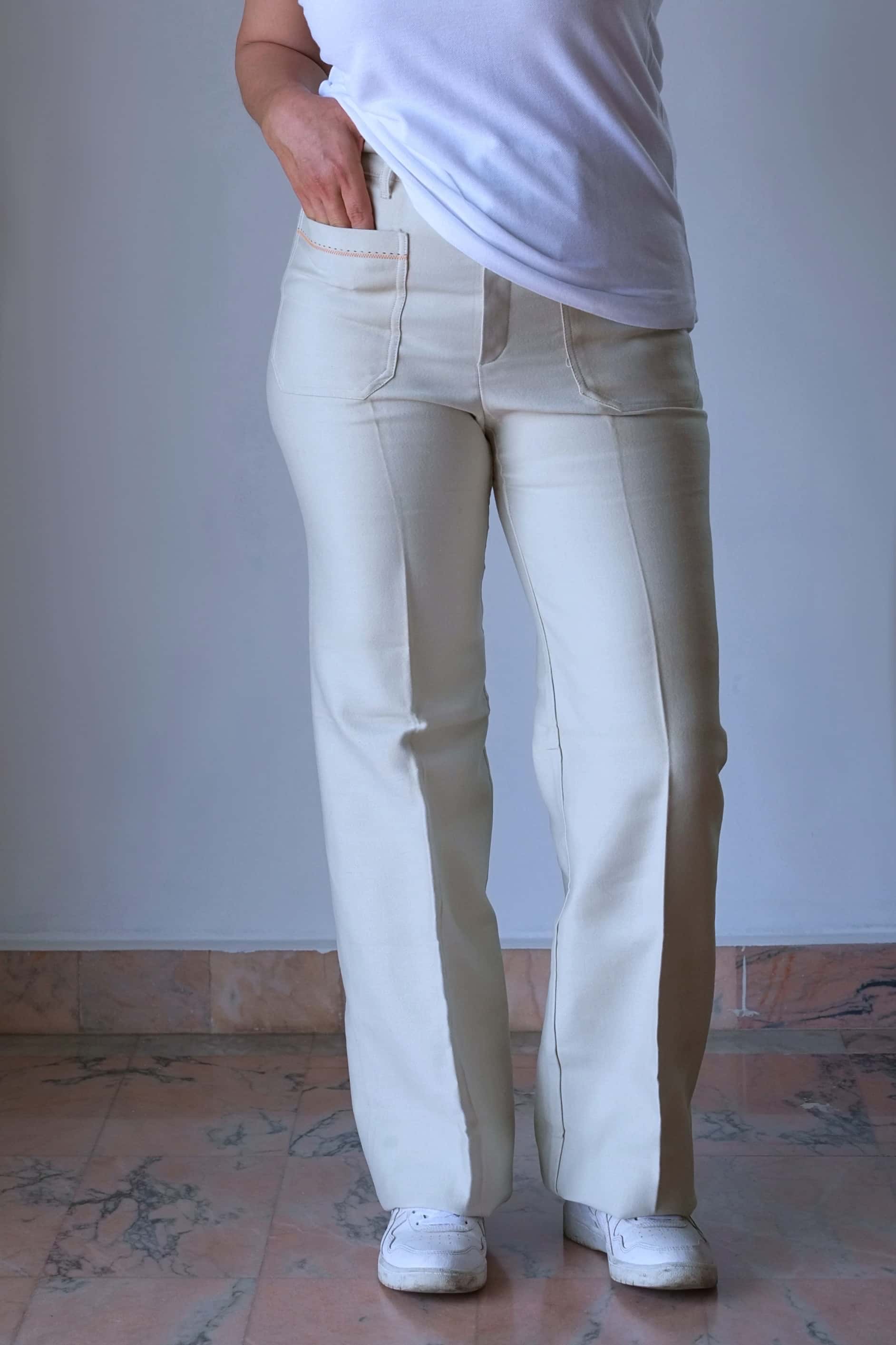 Front view of a model wearing 70's vintage high-waisted cream flared pants and white sneakers.