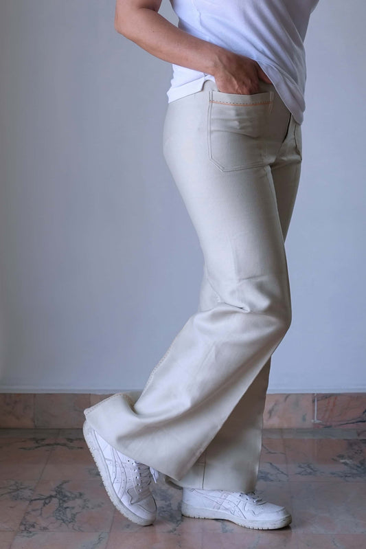 Side view of a model wearing 70's Vintage high-waisted cream flared pants paired with white sneakers, showcasing the vintage design and deep front pockets.