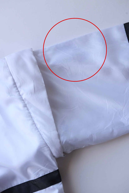 Close-up of white Lacoste track jacket shoulder and sleeve with black trim, showing an area circled in red that highlight imperfections.