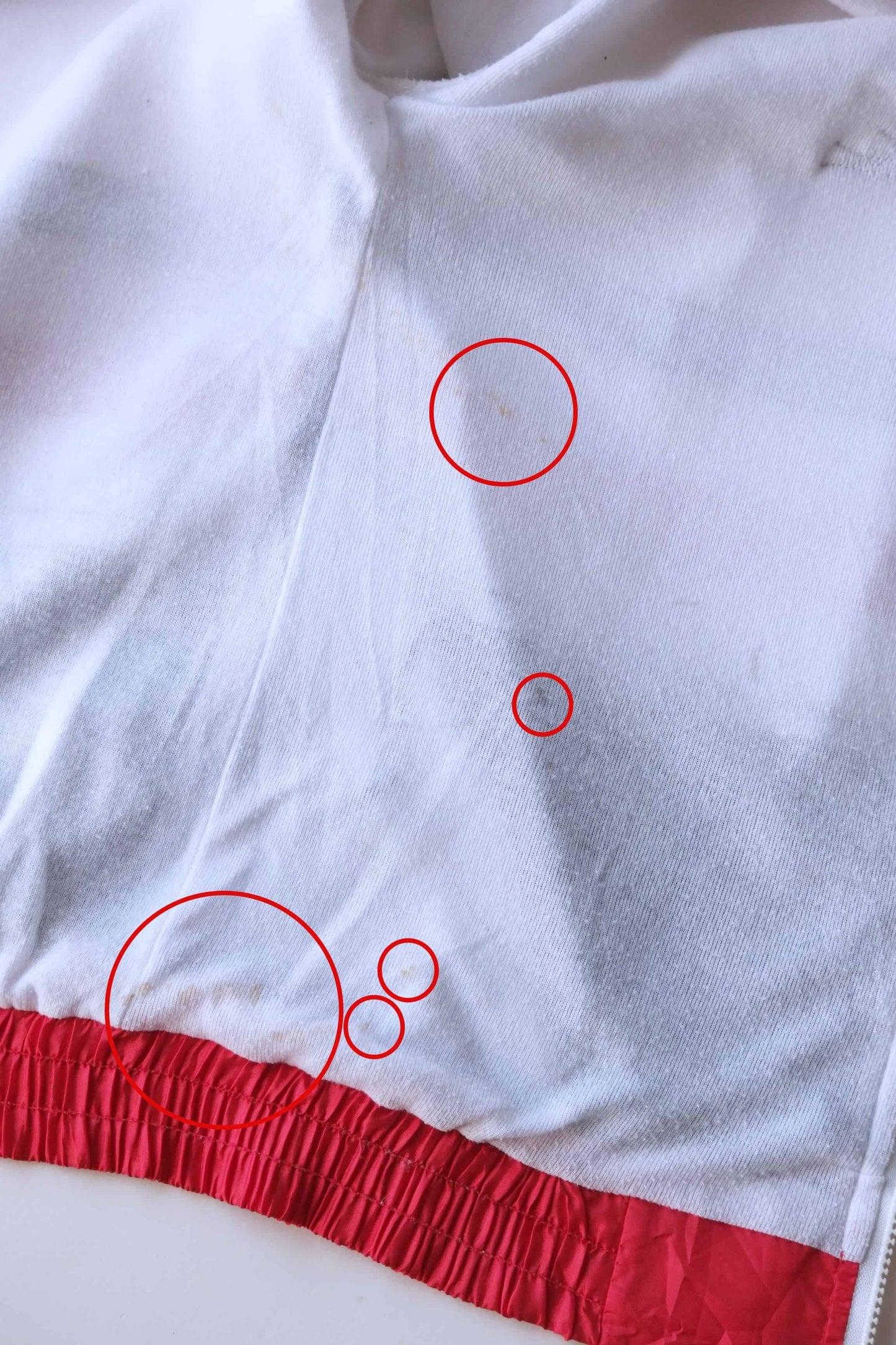 Close-up of the white lining of a Lacoste track jacket red elastic hem, showing several areas circled in red that highlight light stains.