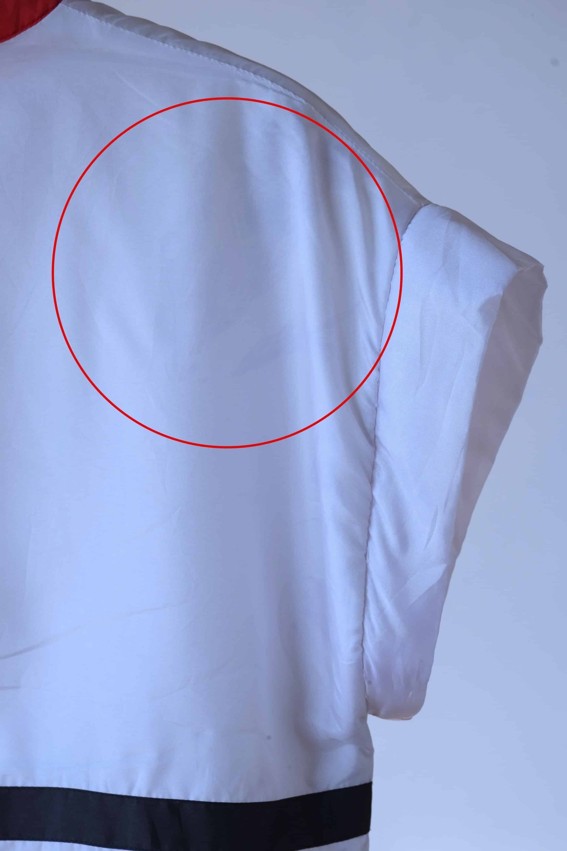 Close-up of the shoulder of a white Lacoste track jacket with black and red trim, showing an area circled in red that highlight fabric imperfections.