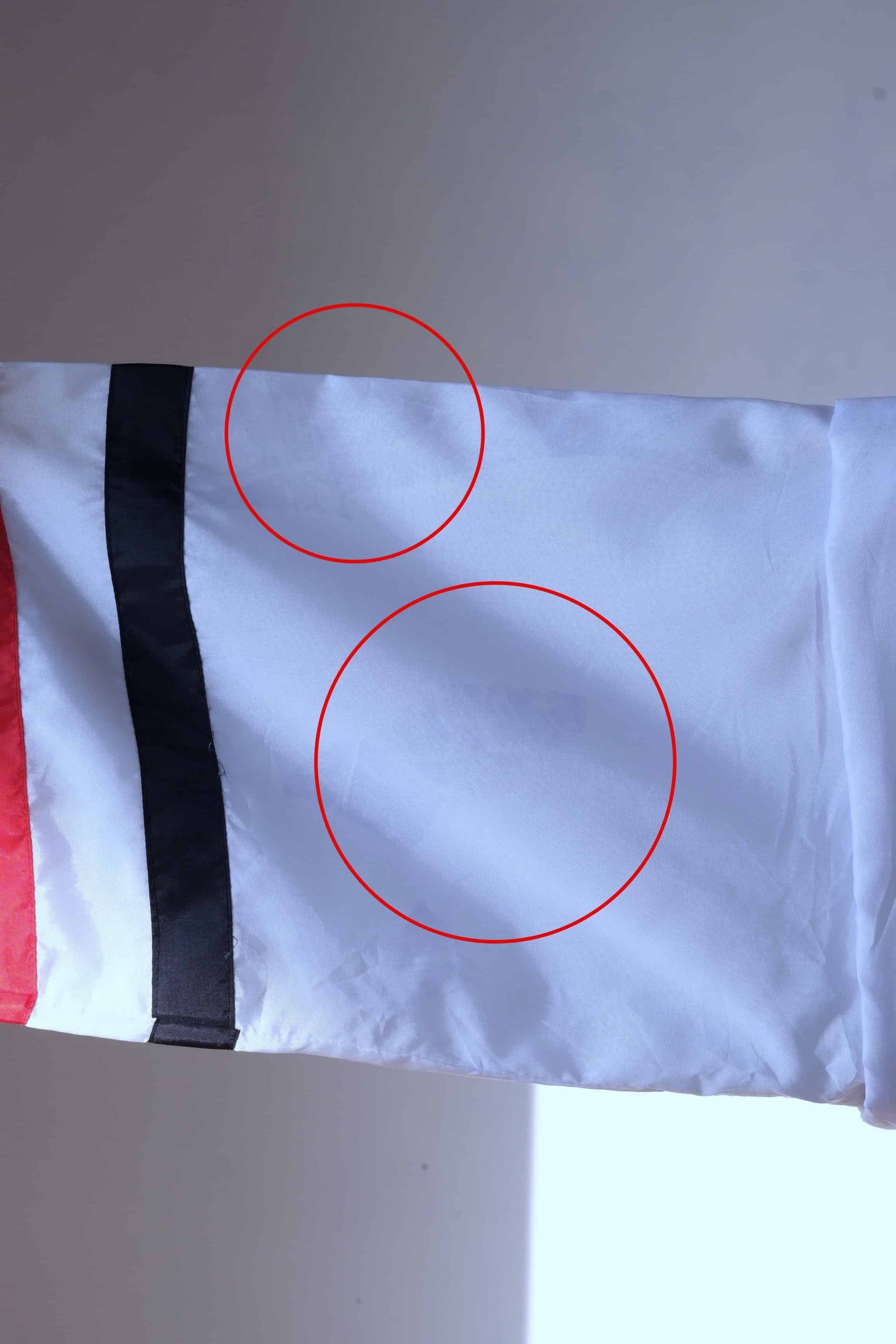 Close-up of white Lacoste track jacket sleeve with black and red trim, showing two areas circled in red that highlight imperfections.