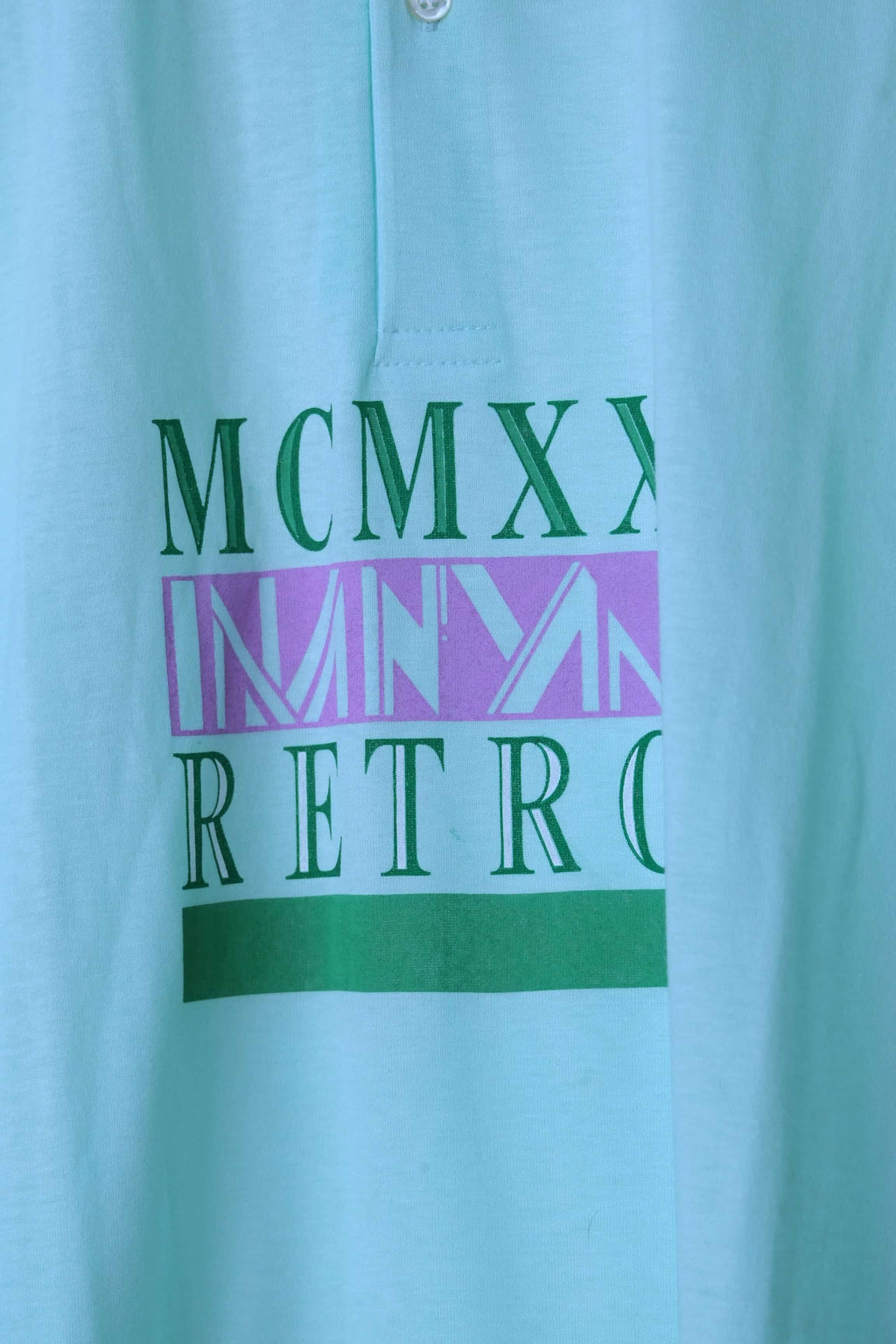 Close-up of the MCMXX Retro graphic on a mint green Löffler 90s polo, with green serif lettering, a lilac band and a solid green bar