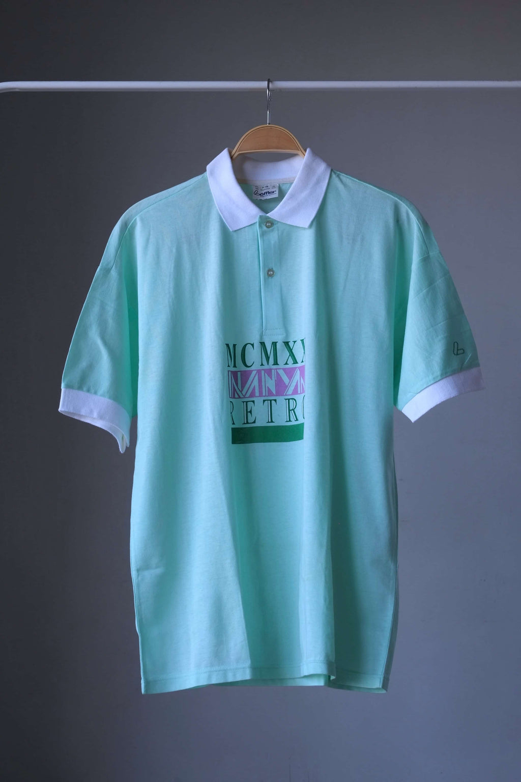 Front view of mint green Löffler 90s men’s short-sleeve tennis polo with white collar and cuffs on a hanger