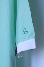 Close-up of white ribbed sleeve cuff and green embroidered Löffler logo on the sleeve of a mint green polo