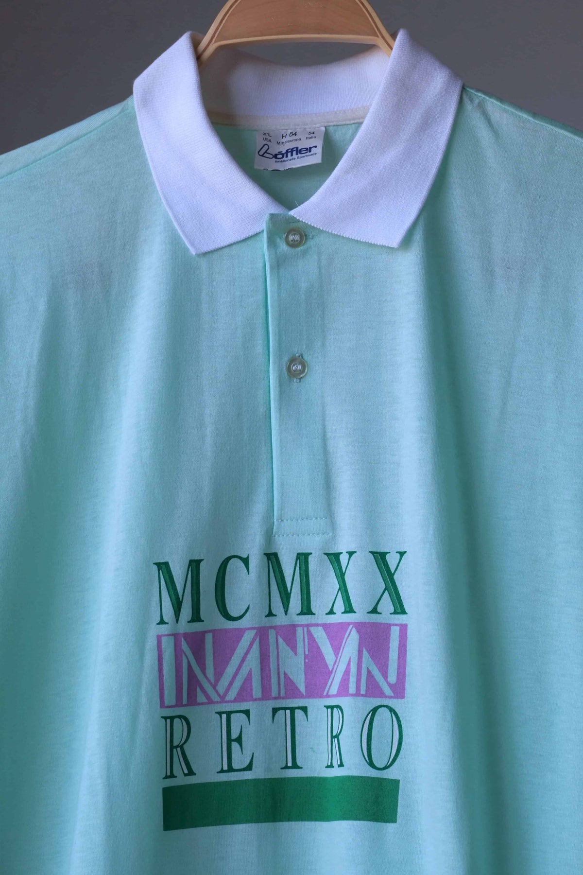 Close-up of mint green Löffler 90s men’s tennis polo with white collar, two-button placket and green and lilac MCMXX Retro graphic