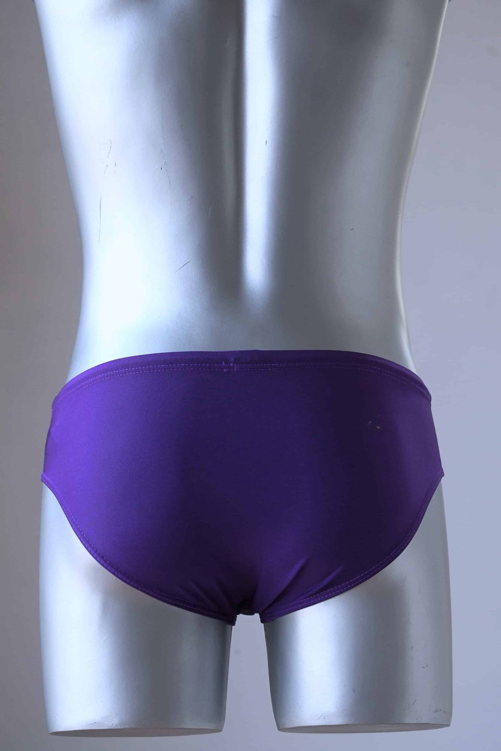Vintage 1980's men's swim briefs in vibrant purple, teal, and grey color block design, worn by a silver mannequin photographed from behind.