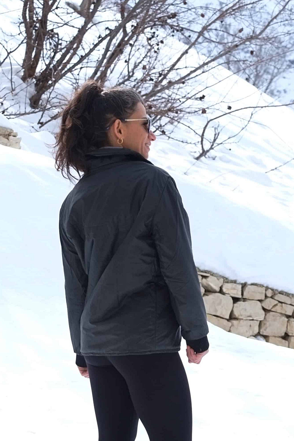 A woman standing in a snowy landscape wearing the vintage black Mossant Rangoon ski jacket, showing the fit and mid-length cut from behind.
