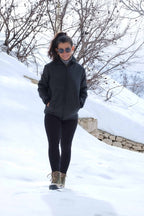 A woman wearing a black 1970s vintage Mossant Rangoon ski jacket with hands in pockets, standing against a bright, snowy mountain background.
